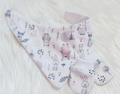 A baby footed blanket and matching booties set in a very pale pink fabric with a whimsical woodland animal print featuring rabbits, owls, a raccoon, a duck, and small floral motifs, displayed on a white faux fur background.