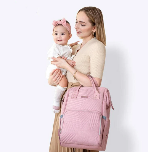 Woman holding a baby and a pink quilted bag against a white background
