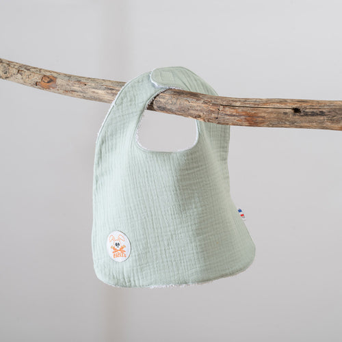 Light green baby bib hanging on a wooden branch against a plain background