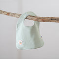 Light green baby bib hanging on a wooden branch against a plain background