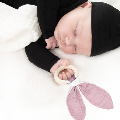 Newborn baby sleeping with a teething ring and pink leaf-shaped blanket
