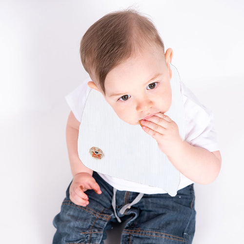 Baby wearing a white bib with a cartoon character on a plain background