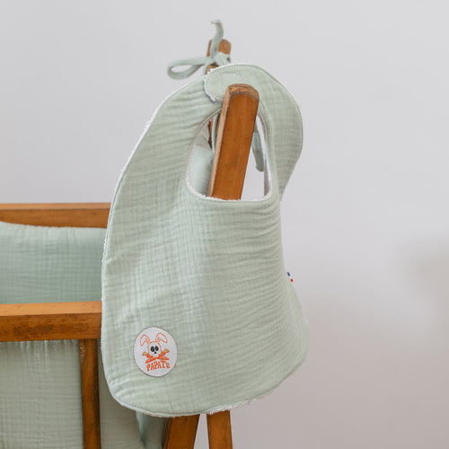 Light green baby bib with a brand logo on a wooden stand against a light gray background