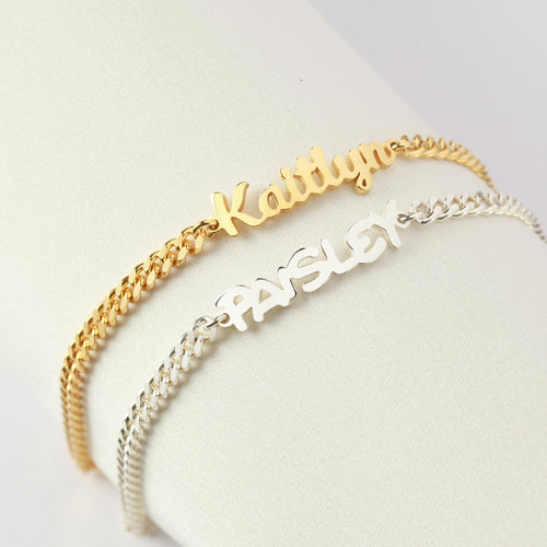 Two gold name bracelets on a white surface