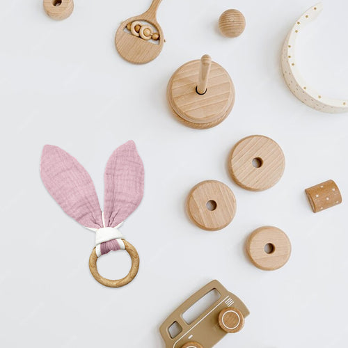 Collection of wooden toys including a pink bunny ear rattle and various shapes on a white background