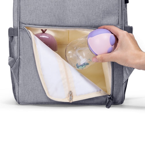 Gray backpack with a hand reaching in to place a purple and white baby bottle inside.