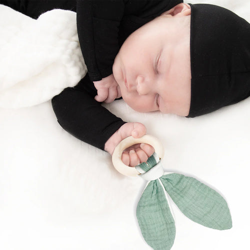 Newborn baby holding a green leaf-shaped teething ring on a white blanket