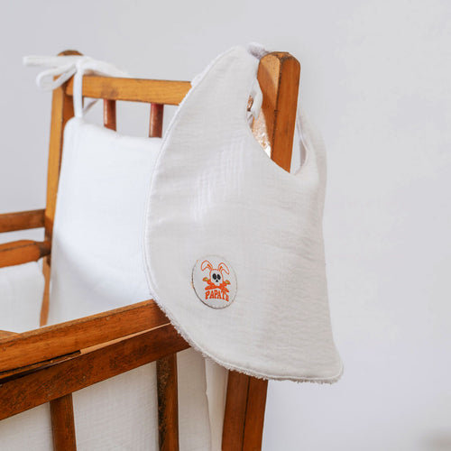 White baby bib with a logo on a wooden chair against a white background