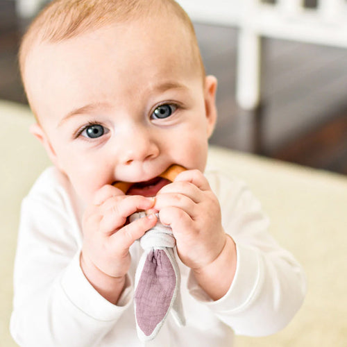 Baby chewing on a purple teething ring with a neutral background