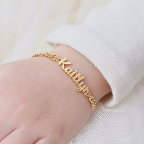 Gold name bracelet on a person's wrist with a white background